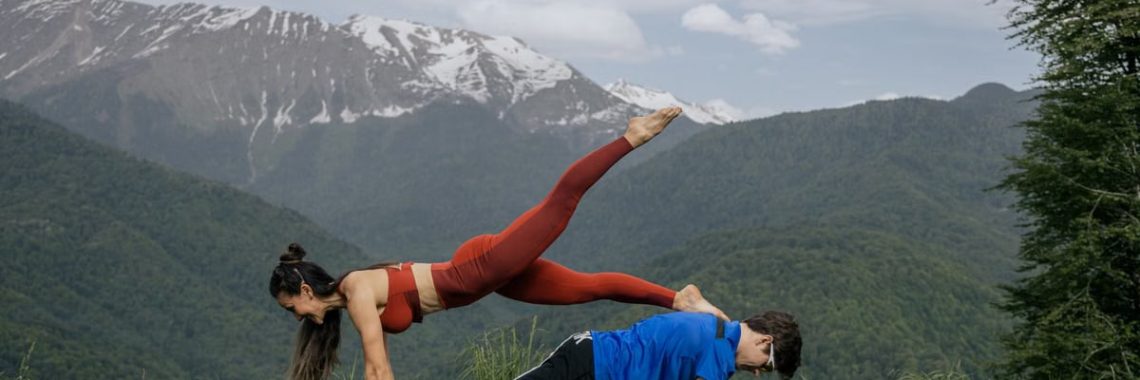 Couple doing yoga exercises outdoors with a breathtaking mountain view.